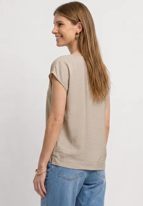 Vrouw van achteren in beige T-shirt en lichtblauwe jeans voor witte achtergrond.
