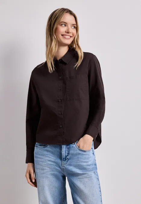 Frau in schwarzem Hemd und blauen Jeans vor neutralem Hintergrund.