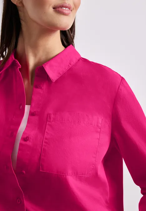 Frau trägt ein leuchtend pinkes Hemd mit Kragen, Knopfleiste und Tasche, darüber ein weißes Top.