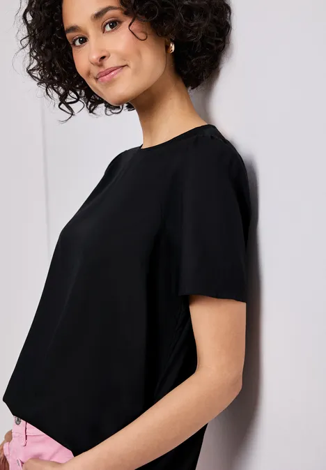 Blouse met ronde hals en korte pofmouwen Black Persoon in profiel tegen een muur, draagt een zwarte top met korte mouwen en een roze broek.