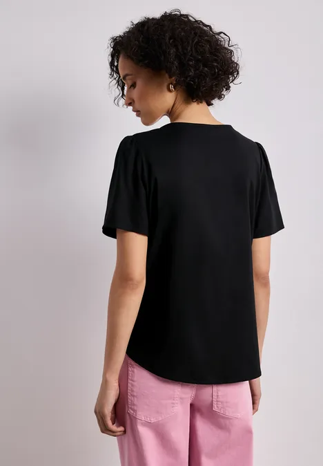 Blouse met ronde hals en korte pofmouwen Black Persoon van achteren met zwart t-shirt en roze broek, krullend haar.