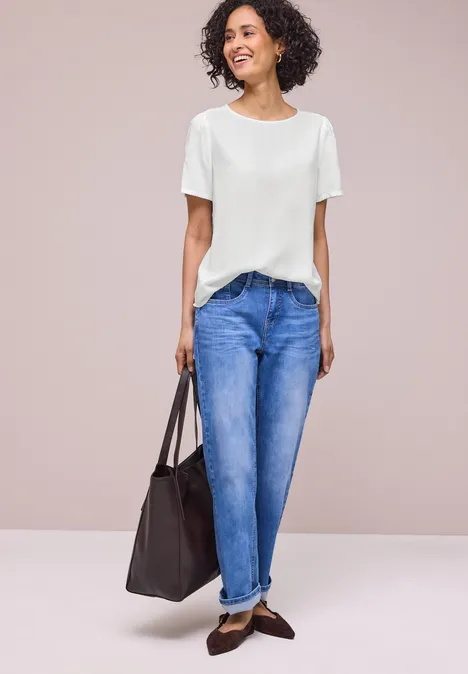 Vrouw met wit T-shirt, blauwe jeans, bruine loafers en een donkere tas.