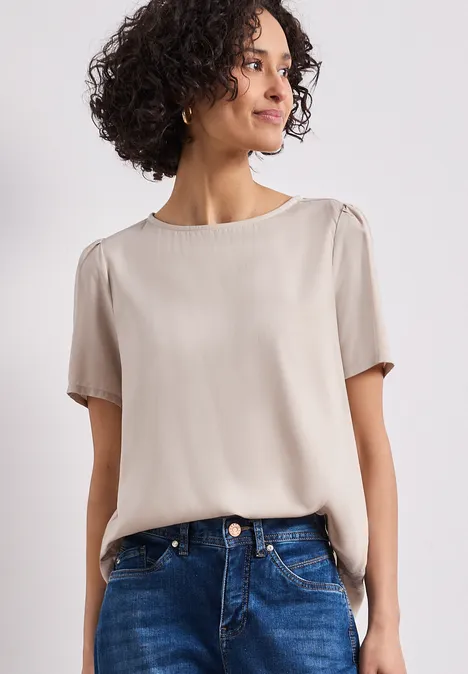 Blouse met ronde hals en korte pofmouwen cotton beige Een vrouw draagt een crème korte mouwen blouse en blauwe jeans tegen een lichte achtergrond.