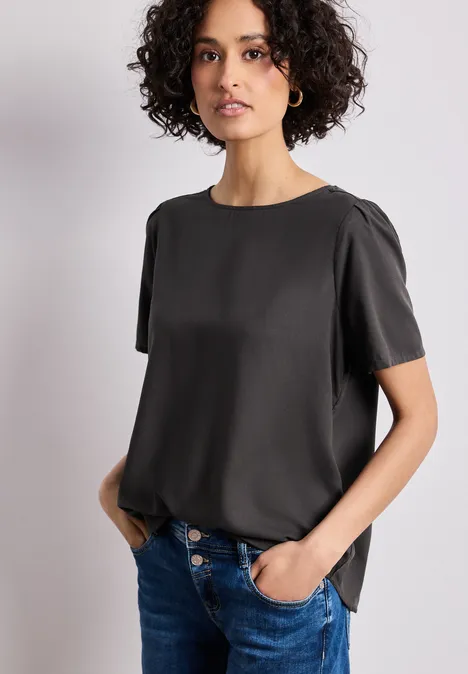 Person mit schwarzem T-Shirt und blauen Jeans, Hände in den Taschen, lockere Passform.