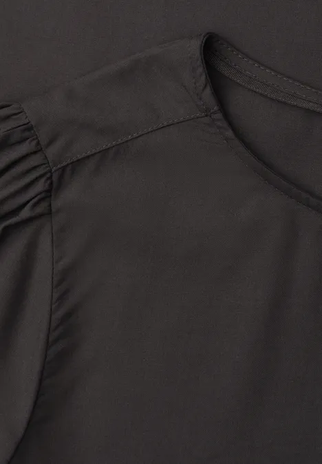 Schwarzes Shirt mit rundem Ausschnitt und dezenten Rüschen-Details an den Schultern.