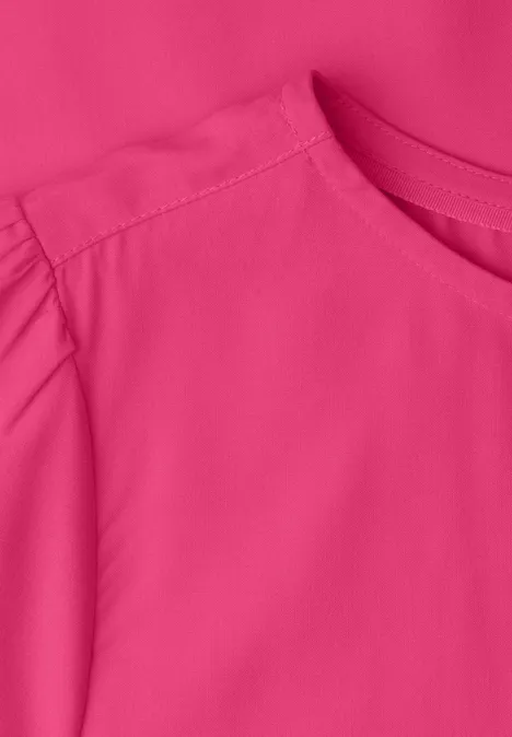 Nahaufnahme eines knallpinken Oberteils mit Rundhalsausschnitt und gerafftem Ärmel.