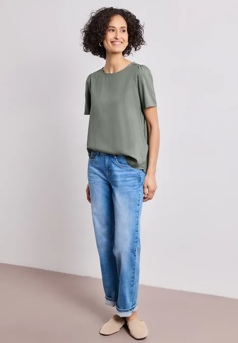 Blouse met ronde hals en korte pofmouwen bound green Persoon draagt loszittend groen T-shirt en wijde blauwe spijkerbroek voor neutrale achtergrond.