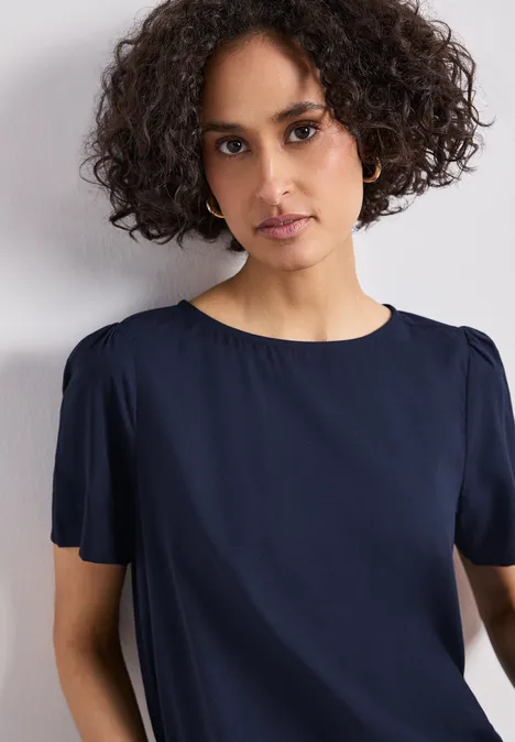 Blouse met ronde hals en korte pofmouwen shadowed navy Een persoon met krullend haar draagt een marineblauw kort mouwtoppie voor een witte achtergrond.
