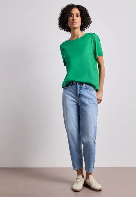 Blouse met ronde hals en korte pofmouwen ever green Een persoon draagt een groen shirt, lichte spijkerbroek en sneakers, staand voor een neutrale achtergrond.