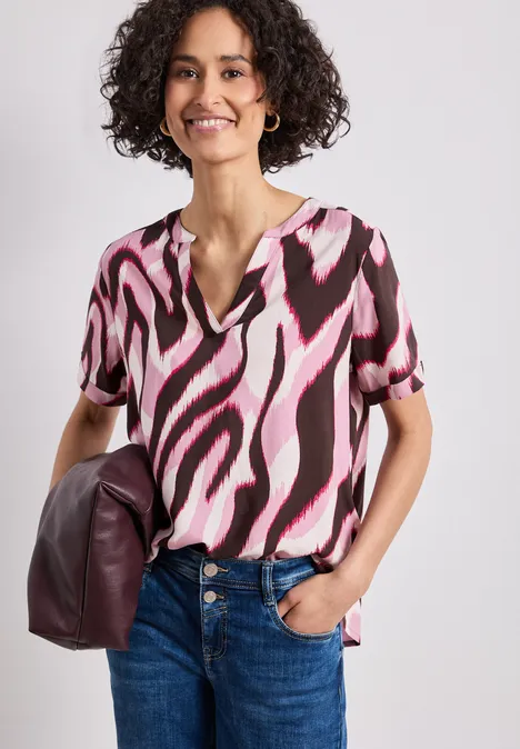 Femme en jean et t-shirt manches courtes à motif rose et noir, tenant un sac bordeaux.