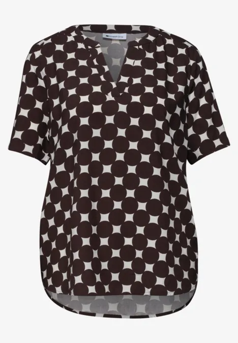 Schwarze Bluse mit weißem Kreismuster, V-Ausschnitt und kurzen Ärmeln.