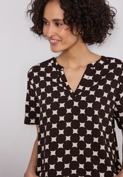 Eine Person trägt eine kurzärmelige Bluse mit schwarzem Hintergrund und weißem Kreismuster.