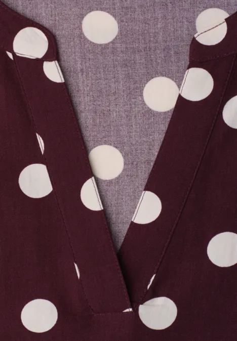 Gros plan d’un haut col V bordeaux à pois blancs.