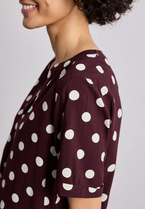 Portrait de profil d'une personne souriante portant un t-shirt bordeaux à pois blancs.