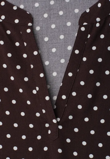 Braunes Polka-Dot-Oberteil mit weiß gepunktetem Muster und V-Ausschnitt.