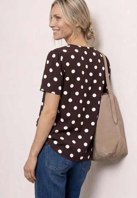 Femme vue de dos portant un haut marron à pois, un jean bleu et un sac en toile beige.