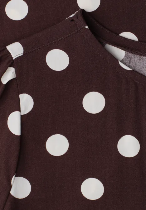 Tissu marron à gros pois blancs avec couture apparente, semblant appartenir à un vêtement avec poche.