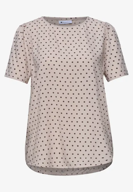 Beige T-shirt met zwarte polkadots en korte mouwen.