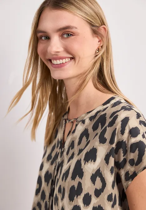 Beige kurzärmlige Bluse mit unregelmäßigem schwarzen Fleckenmuster.