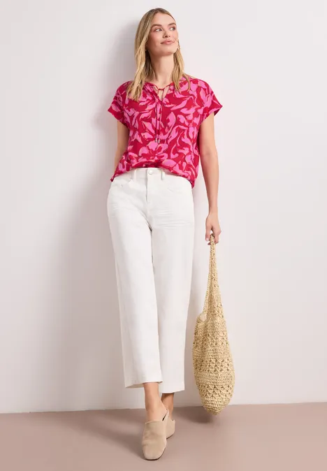 Modell trägt pinkes Shirt mit Muster, weiße Culotte-Jeans, beige Loafers und geflochtene Strohtasche.
