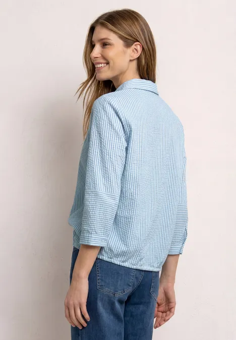 Rugaanzicht van een vrouw in lichtblauw gestreept overhemd met opgerolde mouwen en spijkerbroek.