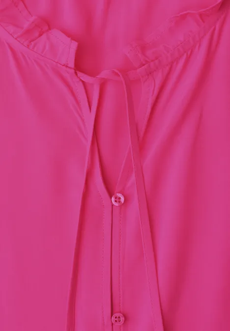 Nahaufnahme einer pinken Bluse mit Rundhalsausschnitt und Knopfleiste.