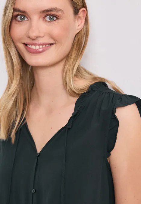 Eine Frau trägt eine ärmellose schwarze Bluse mit Rüschen an den Schultern.