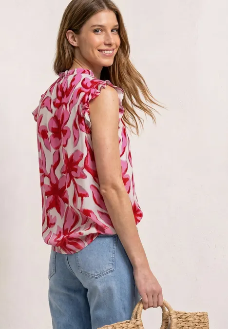Vrouw in roze bloes met bloemenpatroon en blauwe jeans draagt een gevlochten stroentas opzij.