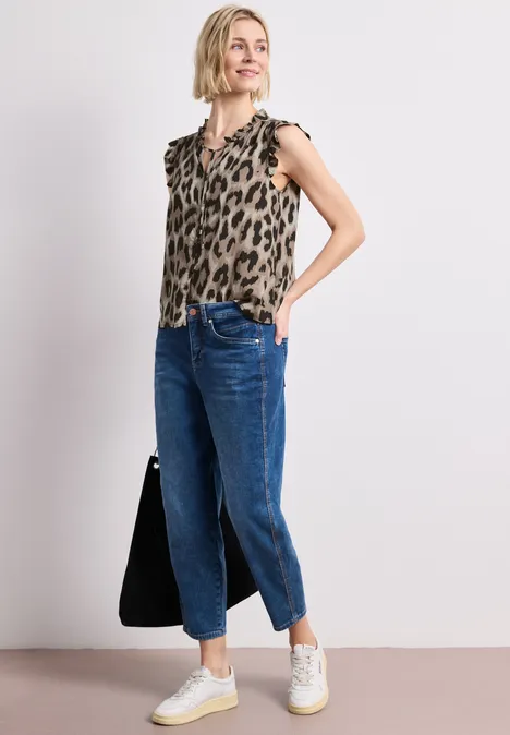 Vrouw in mouwloze leopardprint top, wijde jeans, witte sneakers en een zwarte tas.