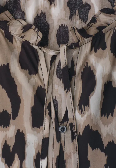 Close-up van een blouse met luipaardprint, knoop en bindbandje bij de hals.