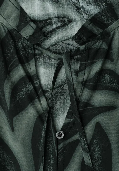 Close-up van een kledingstuk met capuchon, trekkoord en lippenprint in groen-zwart dessin.