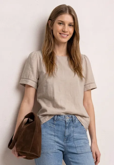 Vrouw in beige T-shirt en spijkerbroek, met een bruine tas.