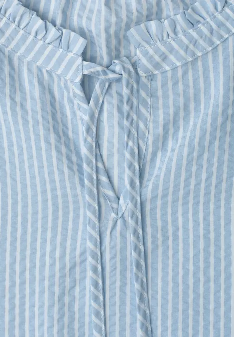 Lichtblauwe blouse met witte strepen en strikje aan de geplooide halslijn.