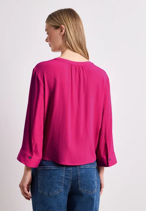 Achteraanzicht van een vrouw in een knalroze blouse en blauwe spijkerbroek.