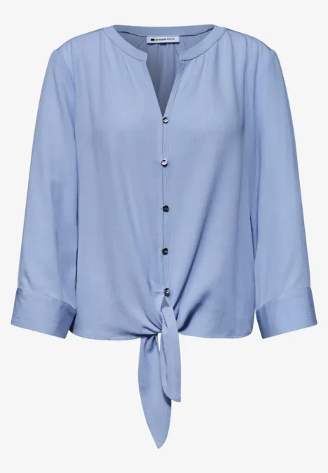 Hellblaue Bluse mit Knopfleiste, 3/4-Ärmeln und Knoten vorne.