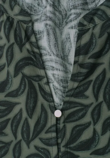 Groen overhemd met donker bladpatroon en centrale knoop onder de V-hals (close-up).