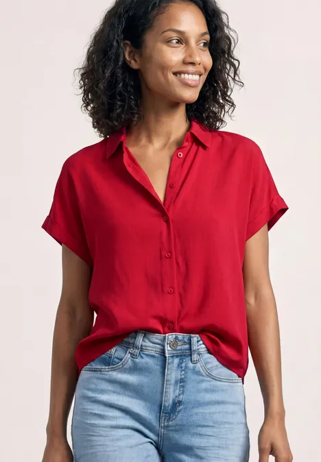 Vrouw in rood kort mouwenhemd, los in lichtblauwe jeans gestopt. Gezicht onscherp.