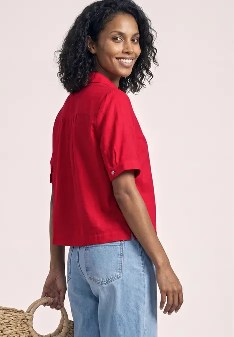 Vrouw in zijaanzicht met krullend haar, in een rood kort shirt en blauwe jeans, met een tas in de hand.