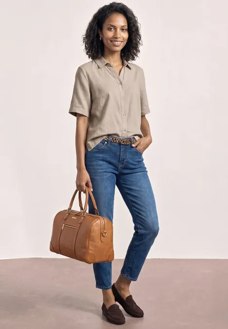Chemisier à manches courtes en couleur unie clay sand Frau in beigefarbenem Hemd und blauen Jeans mit braunen Loafers hält eine braune Lederhandtasche.