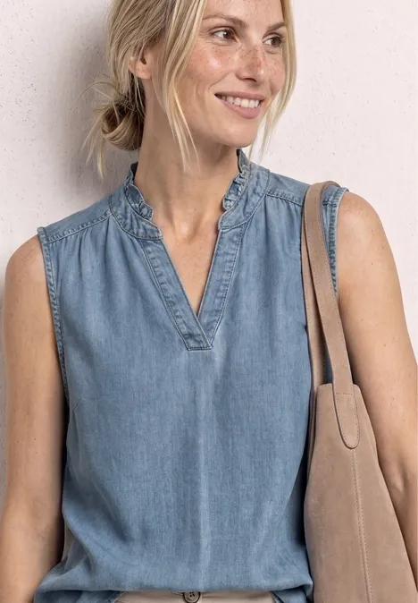 Bovenlichaam van een vrouw in mouwloze spijkerblouse met V-hals, ruches en een schoudertas