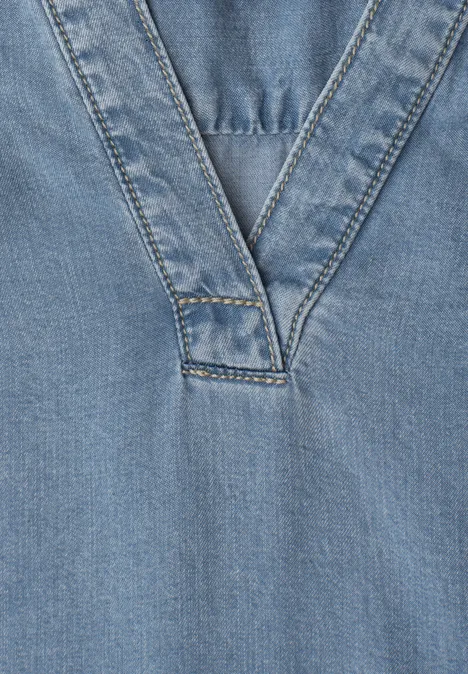 Close-up van een lichtblauw denim top met een opvallende V-neknaad.