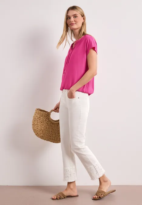 Frau in pinker Bluse und weißen Culotte-Hosen mit Sandalen und geflochtenem Korb.