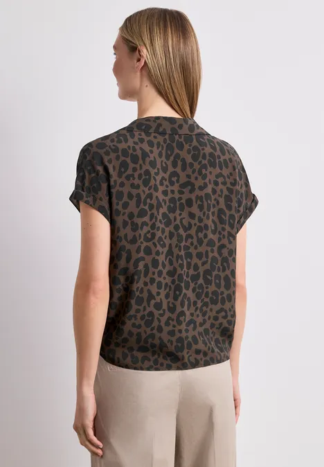 Vrouw van achter in bruin-zwart luipaardprint t-shirt met beige broek, halflang blond haar.
