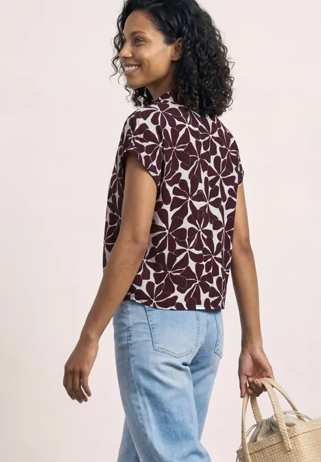 Vrouw van achteren met krullend haar, bloemenprint top, lichtblauwe jeans en gevlochten tas.