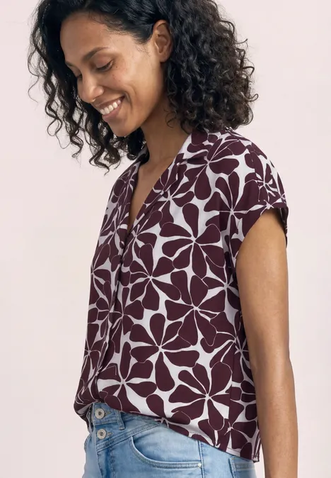 Een persoon in zijaanzicht draagt een bordeauxrode top met grote witte bloemenprint.