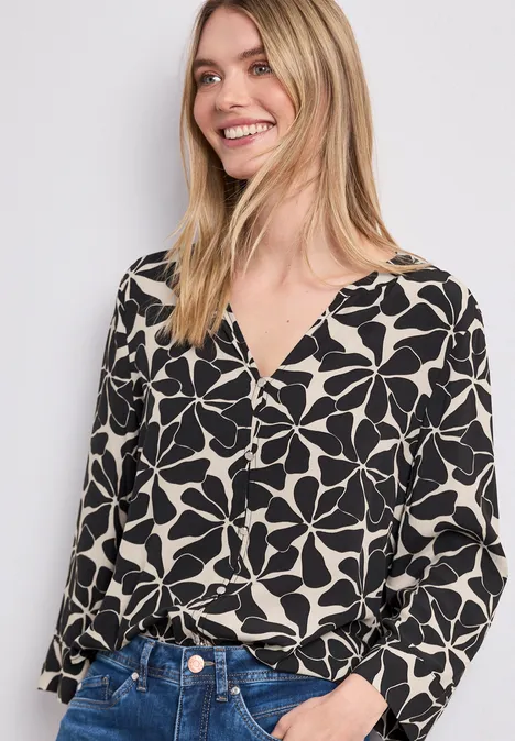 Vrouw in zwart-witte bloes met bloemenprint en blauwe jeans, gezicht onscherp.