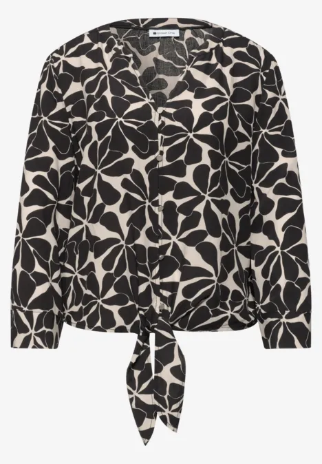Zwart-witte blouse met groot bloemmotief en strik aan de zoom.