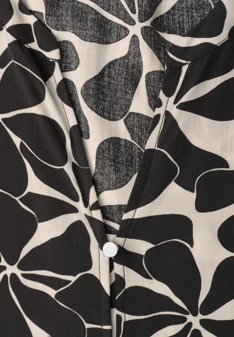 Witte blouse met zwarte, abstracte bloem- en bladpatronen en een zichtbare knoop.