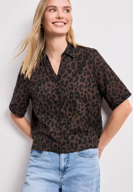 Overhemdblouse met korte mouwen en leopatroon molten earth Frau trägt kurzärmliges, braun-schwarzes Leopardenmuster-Hemd und helle Jeans.
