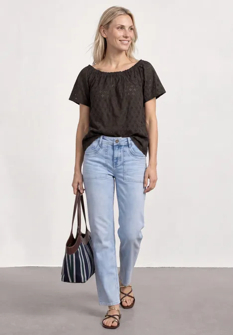 Carmen blouse espresso brown Frau in schwarzem T-Shirt, hellblauen Jeans und Sandalen mit gestreifter Tasche.